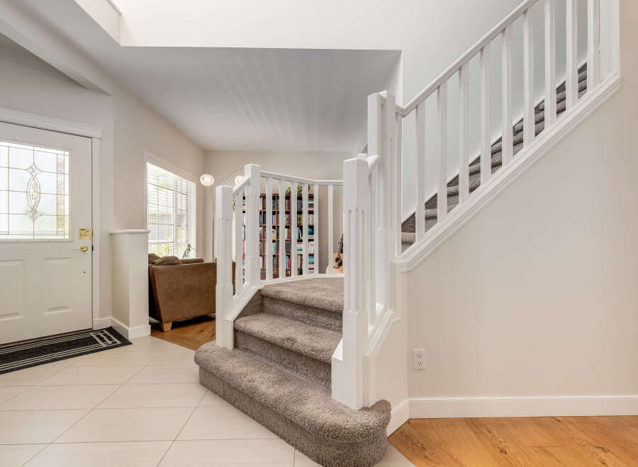 Step into this inviting entryway featuring a bright white door with decorative glass panels, leading to a grand staircase with plush carpeting.