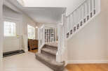 Step into this inviting entryway featuring a bright white door with decorative glass panels, leading to a grand staircase with plush carpeting.
