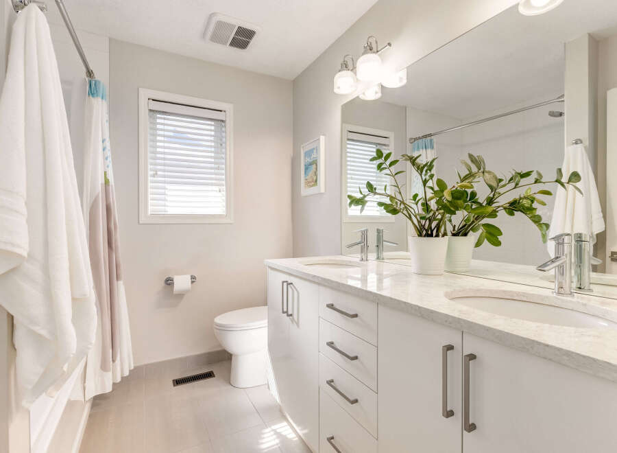 This modern bathroom features a spacious double vanity with sleek white cabinetry and a marble countertop, complemented by two vessel sinks and chrome faucets.