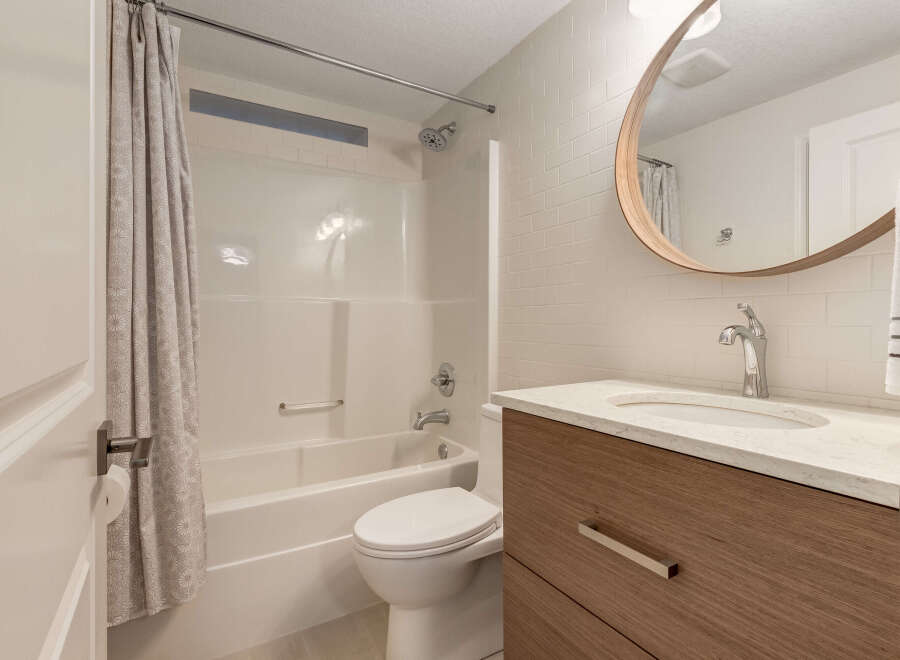 This modern bathroom features a sleek vanity with a marble countertop and a wooden cabinet, complemented by a stylish chrome faucet.