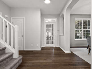 Step into this inviting entryway featuring a grand staircase with plush carpeting and a white banister.