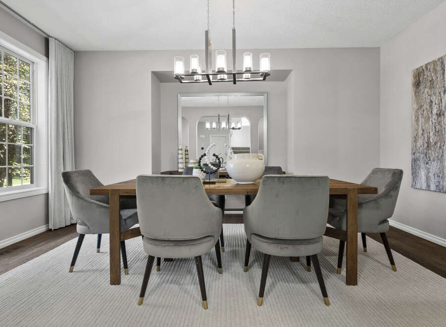 This elegant dining room features a modern rectangular chandelier illuminating a sturdy wooden dining table surrounded by plush grey velvet chairs.