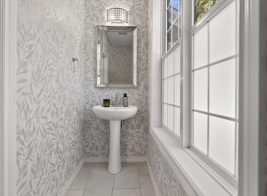 This powder room features elegant leaf-patterned wallpaper and a sleek pedestal sink.