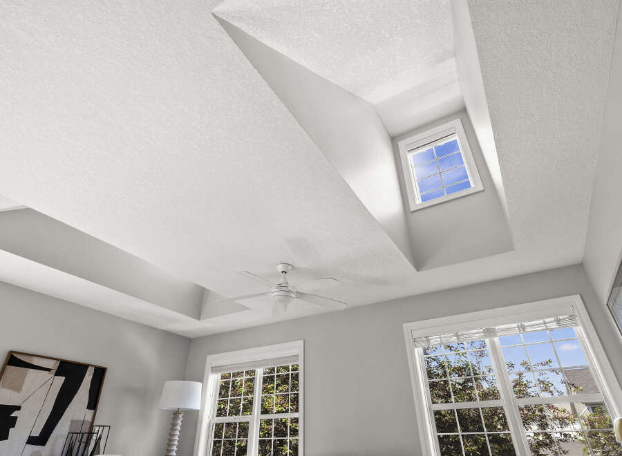 Experience luxury living with this stunning bedroom featuring a dramatic coffered ceiling and a modern ceiling fan.