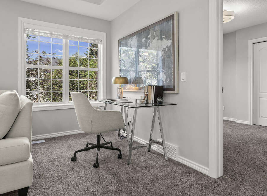 This bright and airy home office features a sleek glass-top desk with chrome legs, complemented by a comfortable upholstered desk chair.