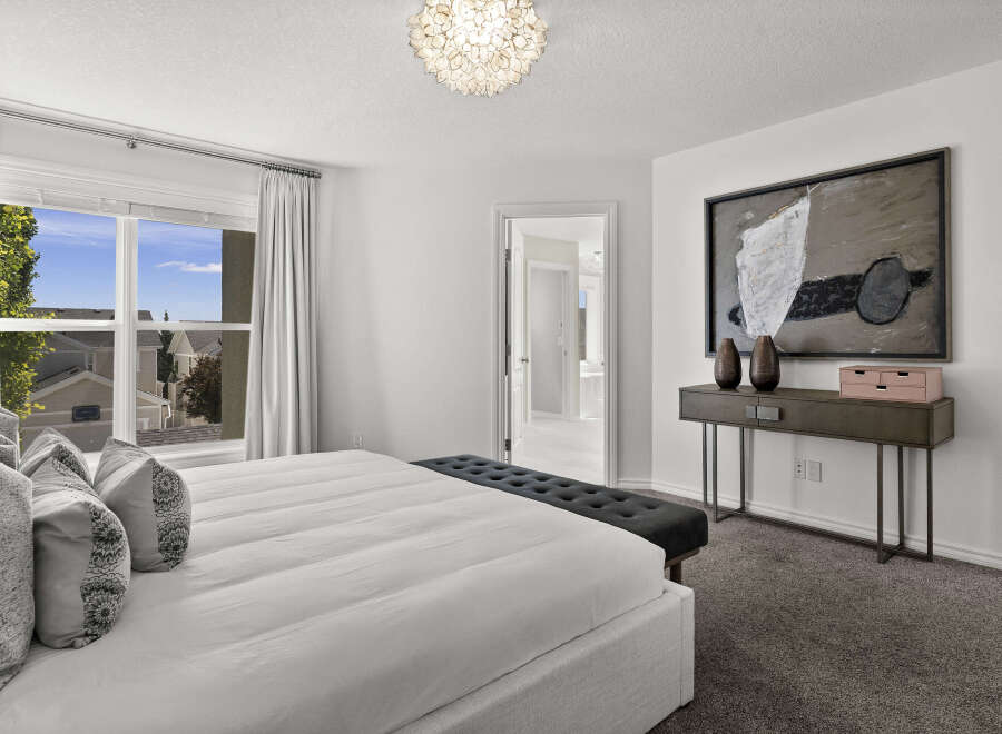 Experience luxury in this master bedroom, featuring a king-sized bed adorned with plush pillows and a stylish tufted bench at the foot.