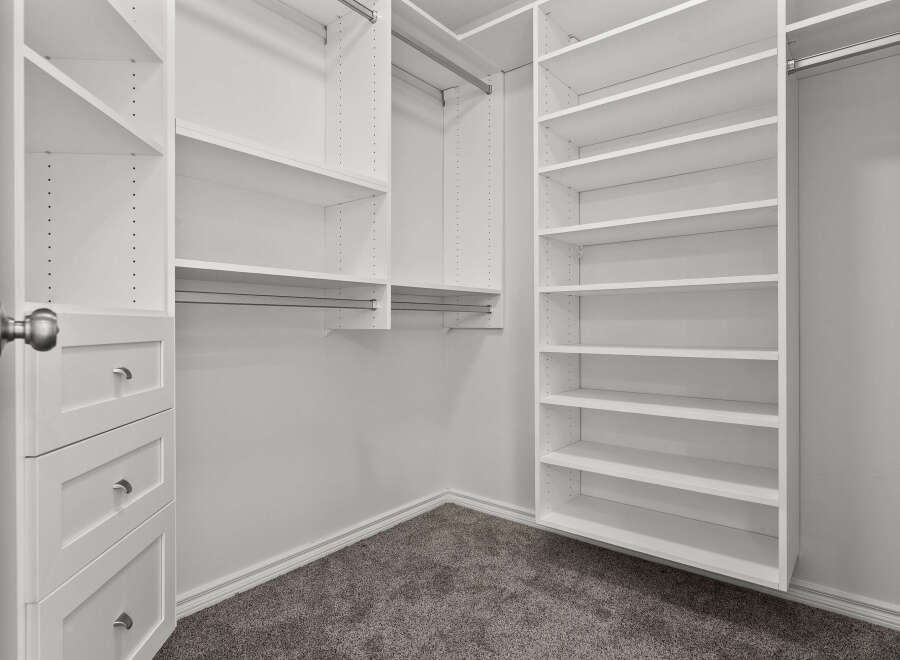 Step into this spacious walk-in closet, featuring ample white shelving and built-in drawers for organized storage.