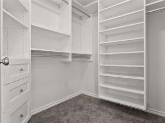 Step into this spacious walk-in closet, featuring ample white shelving and built-in drawers for organized storage.