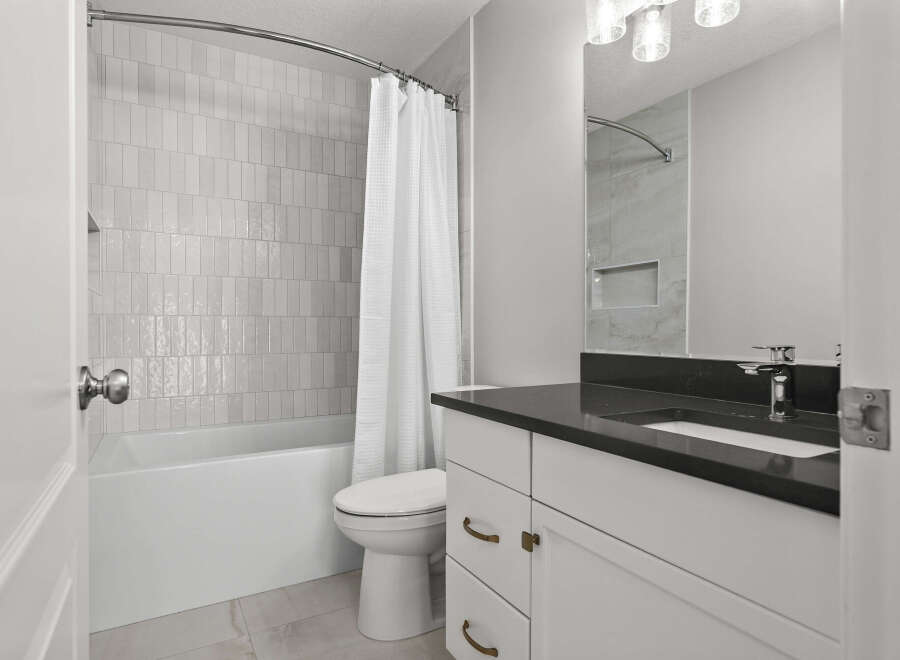 This modern bathroom features a sleek vanity with a dark countertop and brass hardware, complemented by a stylish faucet.