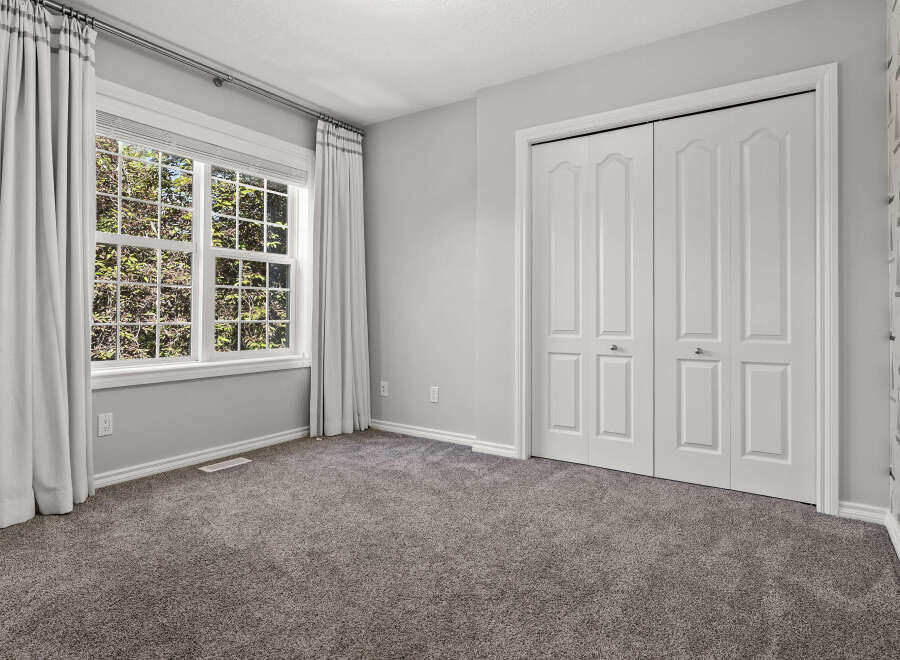 This bedroom features a large window with abundant natural light, complemented by elegant grey curtains.