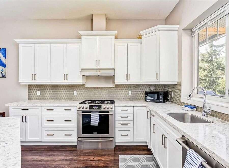 This stunning kitchen boasts sleek white cabinetry and a modern stainless steel gas range, perfect for any home chef.