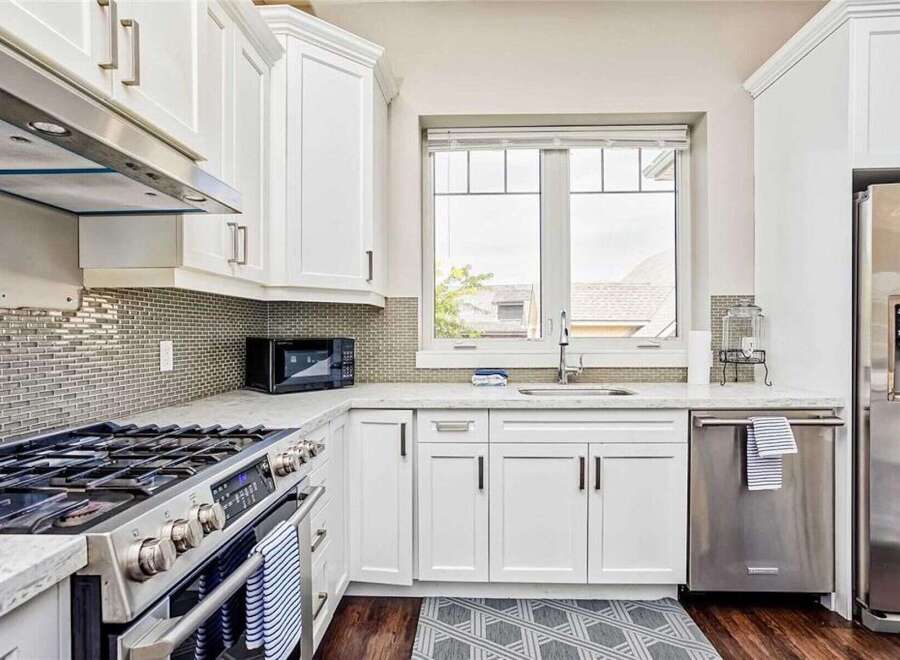 This modern kitchen boasts sleek white cabinetry and a stunning mosaic tile backsplash, complemented by a spacious granite countertop.