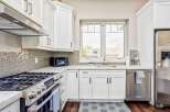 This modern kitchen boasts sleek white cabinetry and a stunning mosaic tile backsplash, complemented by a spacious granite countertop.