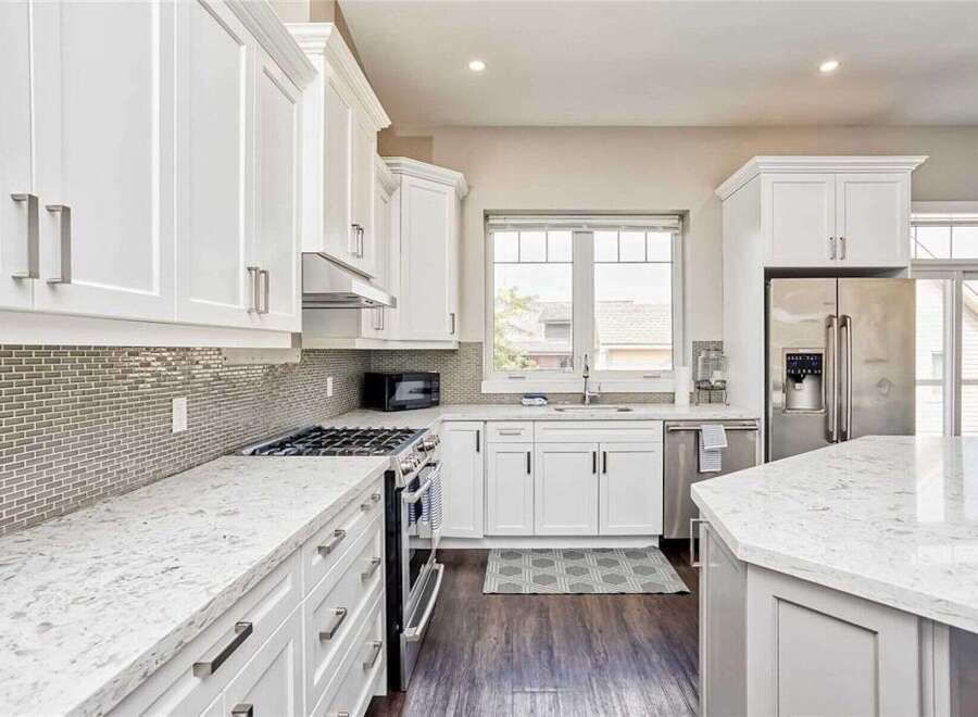 Experience culinary excellence in this stunning modern kitchen, featuring sleek white cabinetry, elegant quartz countertops, and a sophisticated grey mosaic tile backsplash.
