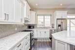 Experience culinary excellence in this stunning modern kitchen, featuring sleek white cabinetry, elegant quartz countertops, and a sophisticated grey mosaic tile backsplash.
