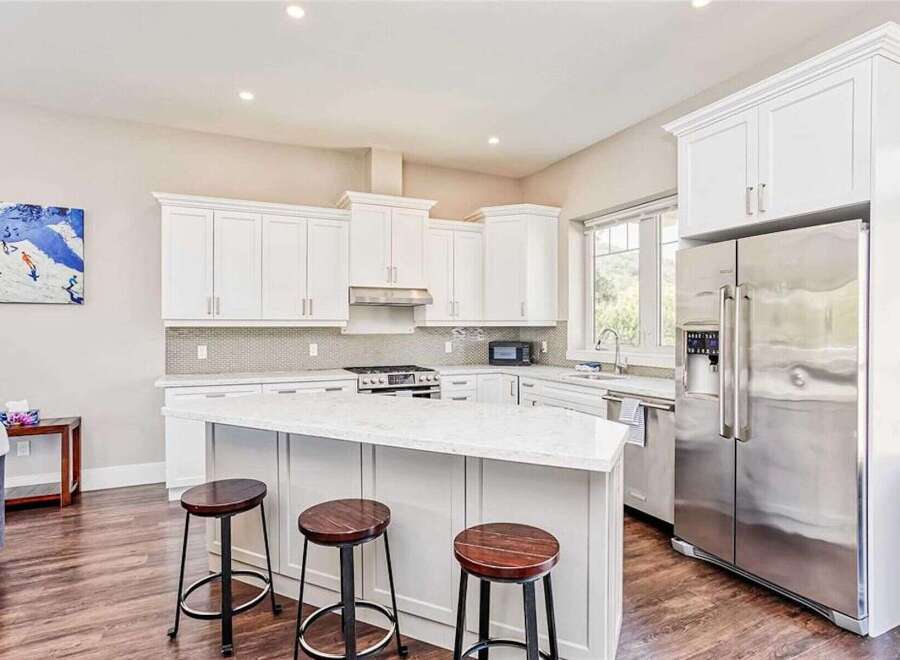 This modern kitchen boasts sleek white cabinetry and a spacious island with a quartz countertop, perfect for casual dining and entertaining.