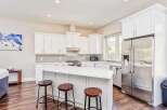 This modern kitchen boasts sleek white cabinetry and a spacious island with a quartz countertop, perfect for casual dining and entertaining.
