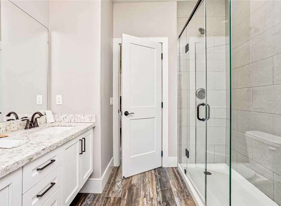This modern bathroom features a sleek vanity with a granite countertop and ample storage, complemented by a spacious glass-enclosed shower with elegant tilework.
