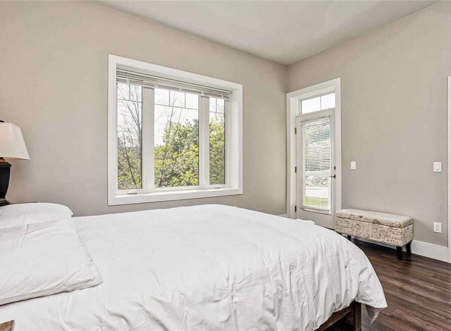 Experience comfort and natural light in this inviting bedroom, featuring a plush white duvet and a large window overlooking lush greenery.
