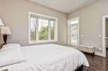 Experience comfort and natural light in this inviting bedroom, featuring a plush white duvet and a large window overlooking lush greenery.
