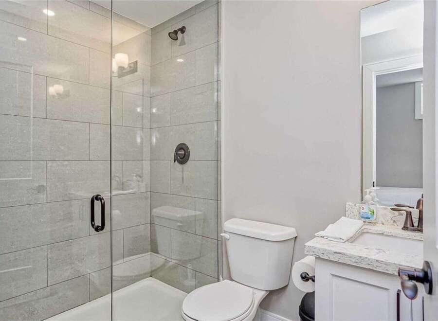 This modern bathroom features a sleek glass-enclosed shower with stylish tile work, complemented by a clean white toilet and a granite-top vanity.