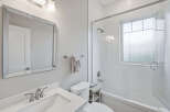 This bright and modern bathroom features a sleek vanity with a silver faucet, a clean white toilet, and a spacious bathtub with a glass enclosure.