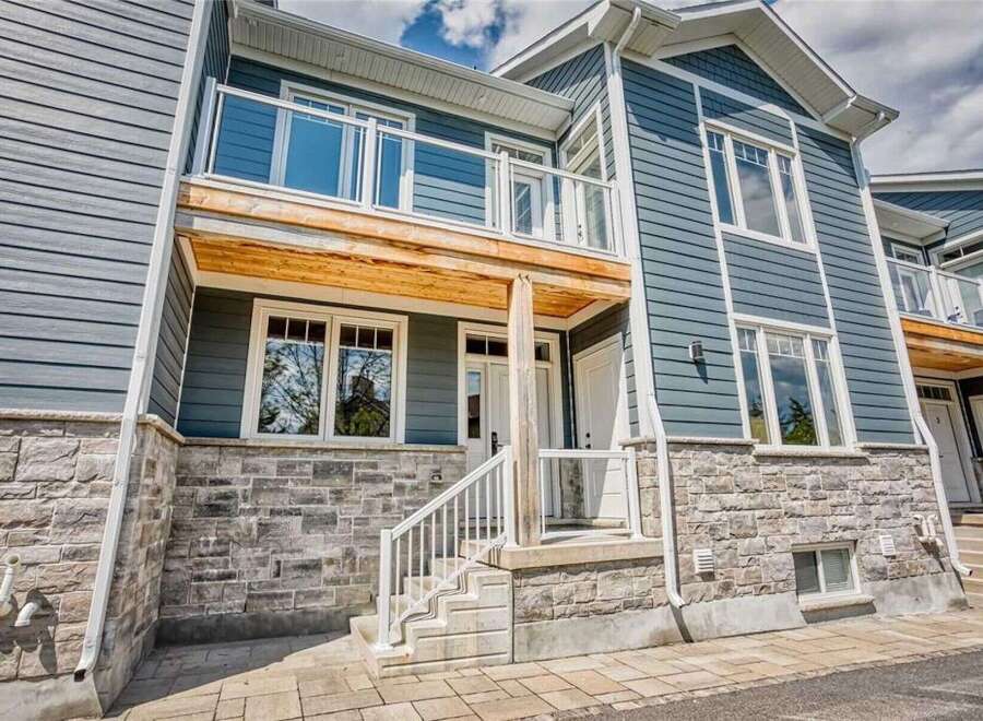 Discover modern living in this stunning townhouse featuring a sleek blue siding exterior complemented by a stone base and a charming wooden balcony.