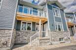Discover modern living in this stunning townhouse featuring a sleek blue siding exterior complemented by a stone base and a charming wooden balcony.