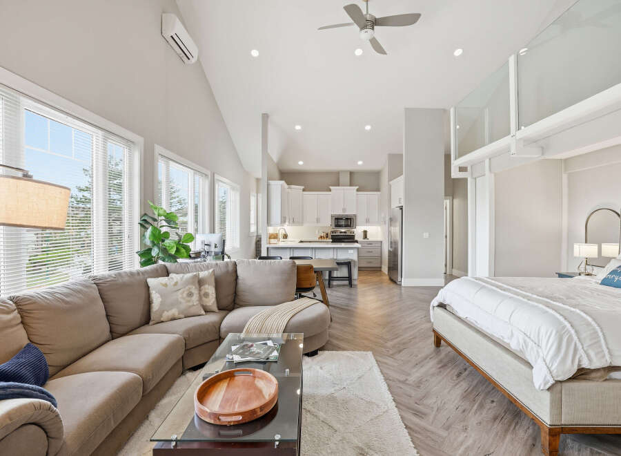 Experience modern living in this open-concept studio featuring a spacious sectional sofa, a sleek kitchen with ample cabinetry, and a comfortable king-sized bed.