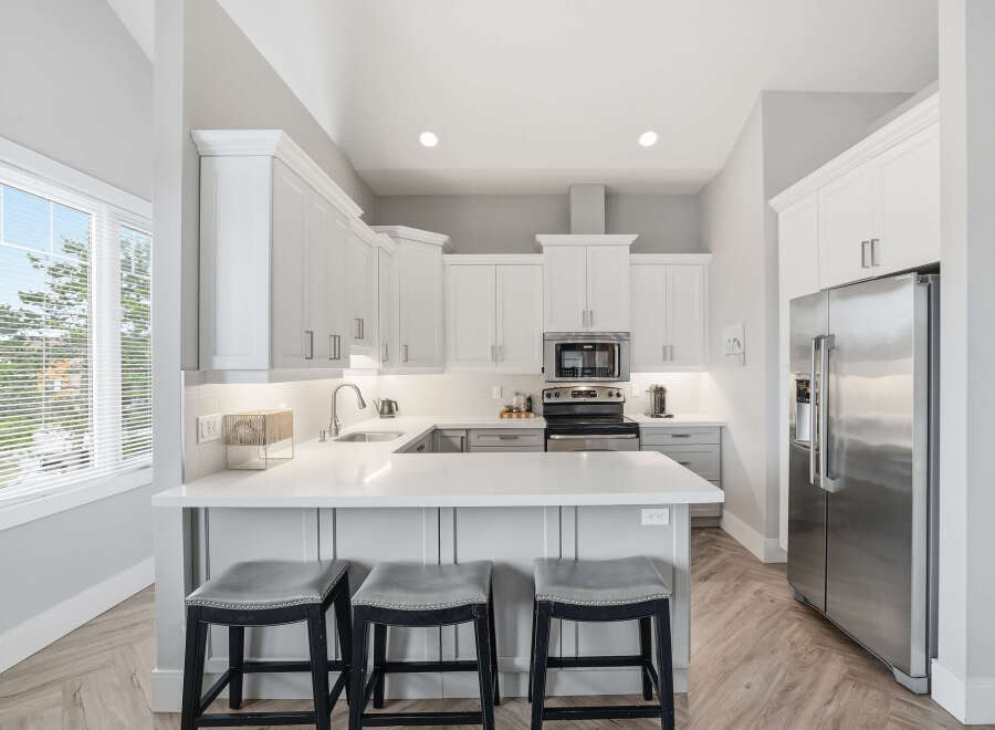 Experience modern living in this stunning kitchen featuring sleek white cabinetry, a spacious quartz countertop island with bar seating, and top-of-the-line stainless steel appliances.