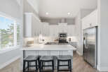 Experience modern living in this stunning kitchen featuring sleek white cabinetry, a spacious quartz countertop island with bar seating, and top-of-the-line stainless steel appliances.