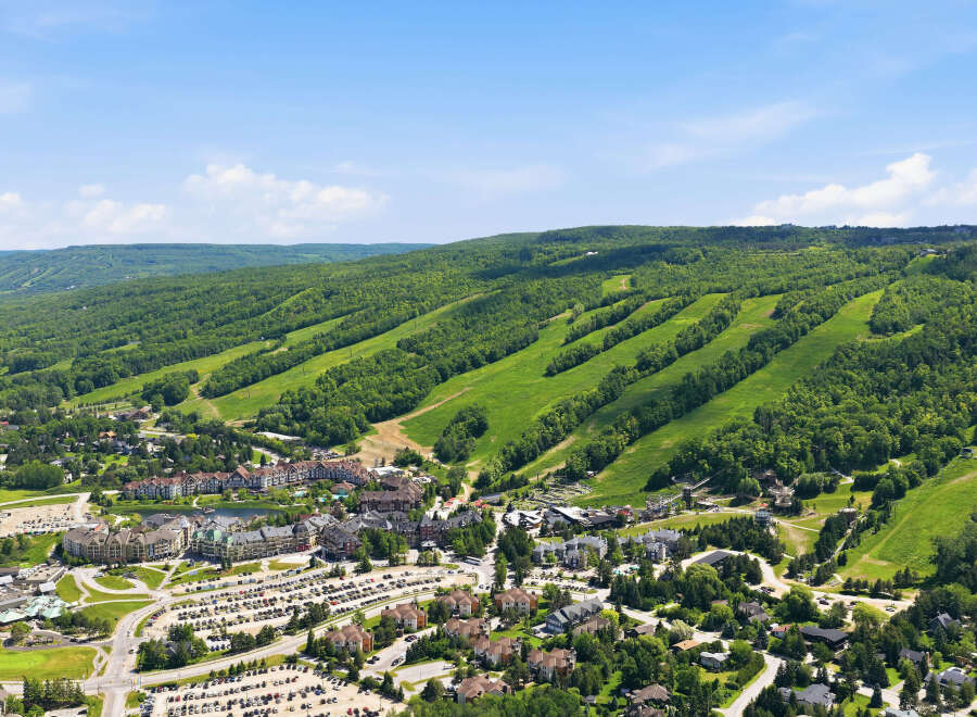 Experience the ultimate mountain lifestyle with this stunning aerial view of a vibrant ski resort village nestled against lush green hills.