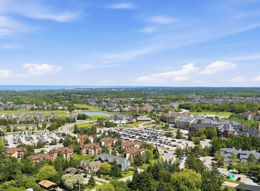 Discover this stunning aerial view of a picturesque resort community, showcasing a harmonious blend of residential buildings, lush green spaces, and a serene lake.