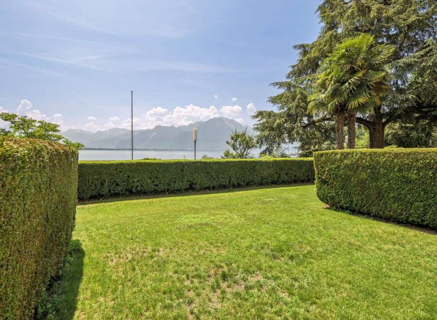 Enjoy breathtaking lake and mountain views from this stunning property, framed by meticulously manicured hedges and lush green lawns.