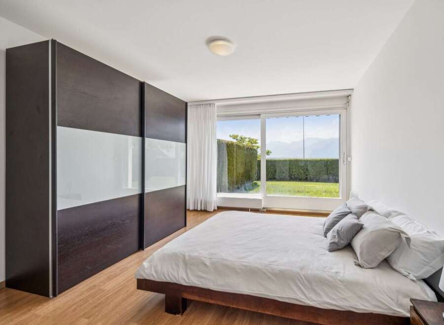 Experience modern living in this serene bedroom featuring a spacious dark wood wardrobe with frosted glass panels.