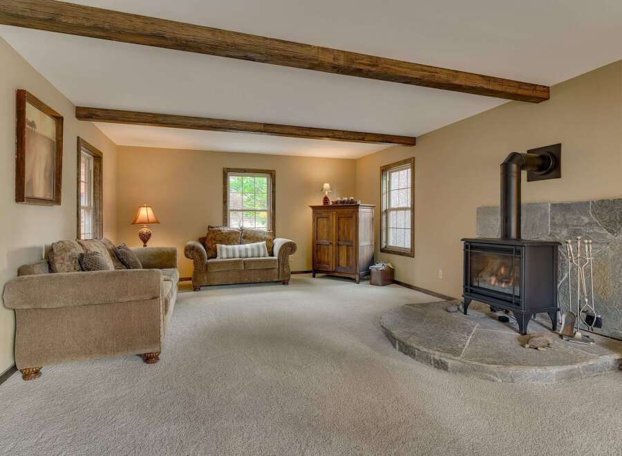 Cozy living room featuring a stone fireplace with a wood-burning stove, complemented by exposed wooden beams on the ceiling.