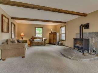 Cozy living room featuring a stone fireplace with a wood-burning stove, complemented by exposed wooden beams on the ceiling.