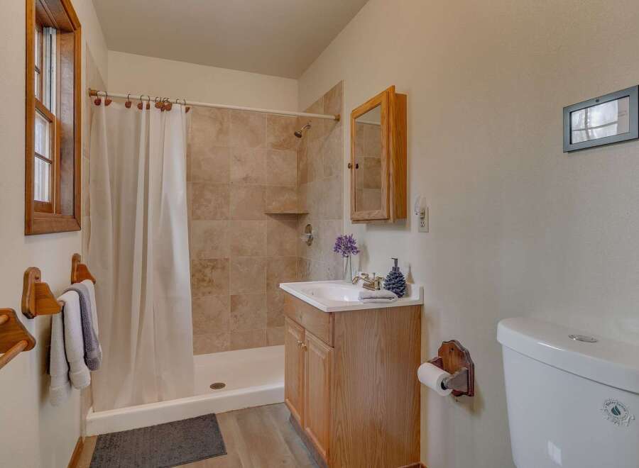 This charming bathroom features a tiled shower with a white curtain, a wooden vanity with a sink, and a toilet.