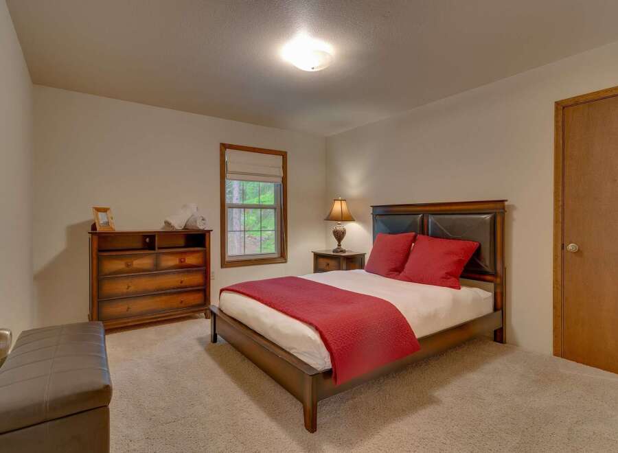 This inviting bedroom features a comfortable queen-size bed adorned with plush red pillows and a matching quilted throw.