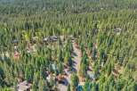 Nestled within a dense forest, this aerial view showcases a charming neighborhood with multiple homes scattered amongst tall pine trees.