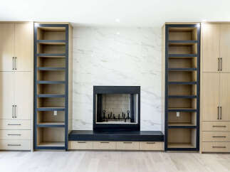 This modern living room features a stunning marble fireplace as the focal point, flanked by custom built-in shelving and cabinetry.