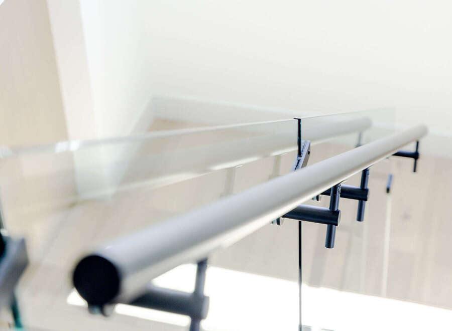 Experience modern living with this stunning staircase featuring a sleek glass railing and a minimalist metal handrail.