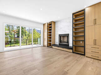 Experience modern living in this spacious room featuring a sleek fireplace with a marble accent wall and custom built-in cabinetry.