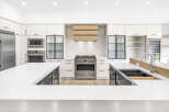 Experience luxury in this modern kitchen, featuring sleek white cabinetry, a professional-grade gas range, and a stunning wood-accented range hood.