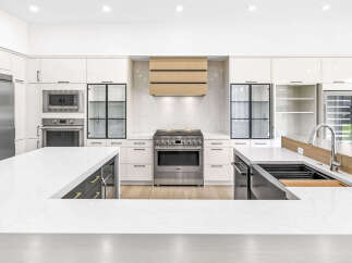 Experience luxury in this modern kitchen, featuring sleek white cabinetry, a professional-grade gas range, and a stunning wood-accented range hood.