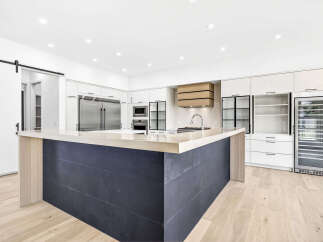 Experience modern luxury in this stunning kitchen, featuring a sleek dark tiled island with a light wood countertop and a matching range hood.