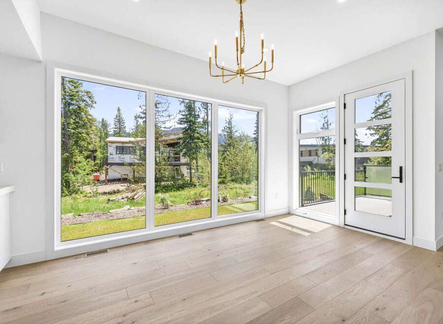 Experience modern living with expansive windows offering breathtaking views of the surrounding nature and a home under construction.