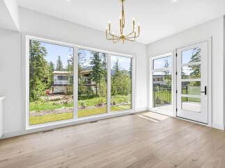 Experience modern living with expansive windows offering breathtaking views of the surrounding nature and a home under construction.