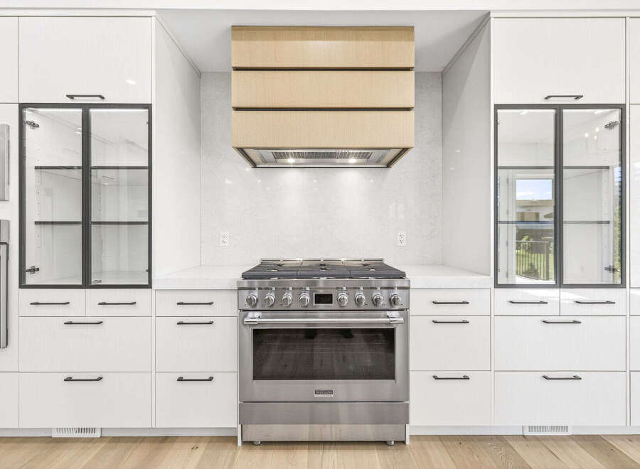 Experience culinary excellence in this modern kitchen, featuring a professional-grade gas range and a sleek, integrated range hood with a warm wood finish.