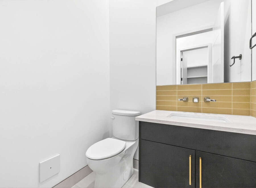 This modern bathroom features a sleek vanity with gold hardware and a white countertop, complemented by a stylish tiled backsplash.